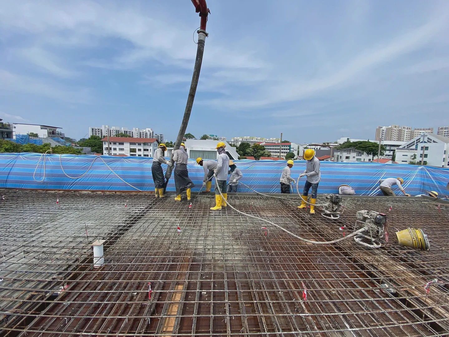 Construction workers pouring concrete foundation, a key stage that influences landed house construction cost in Singapore.